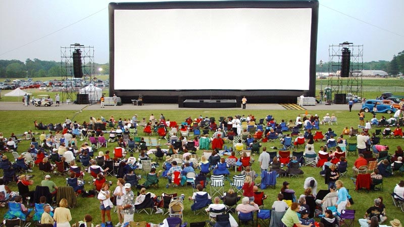 A crowd sitting in front of an outdoor movie screen