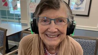 An elderly woman smiles wearing a pair of Silent Sound System headphones