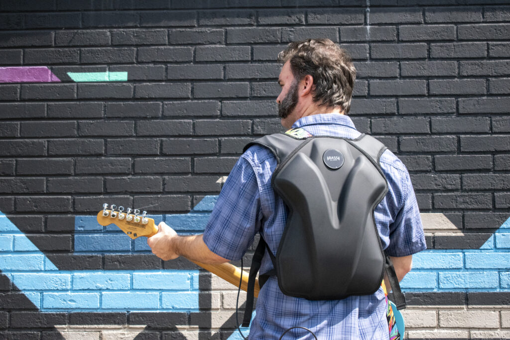 BASSpak On Stage Monitoring Man stands with BASSpak while playing electric guitar in front of a mural